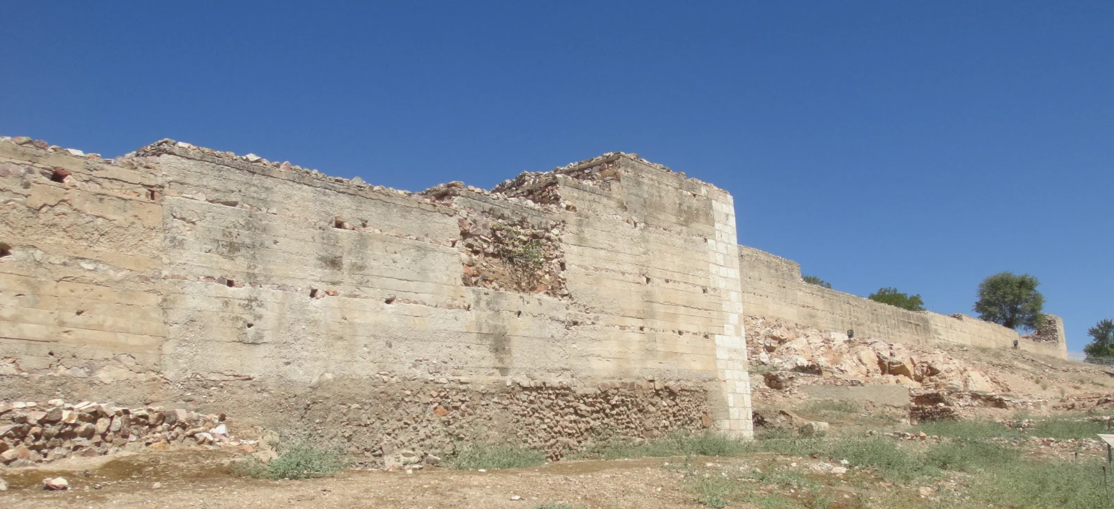 Tramo conservado de la muralla de Alarcos, con una torre saliente y restos de mampostería en su base.